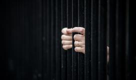 Des mains derrière des barreaux de prison